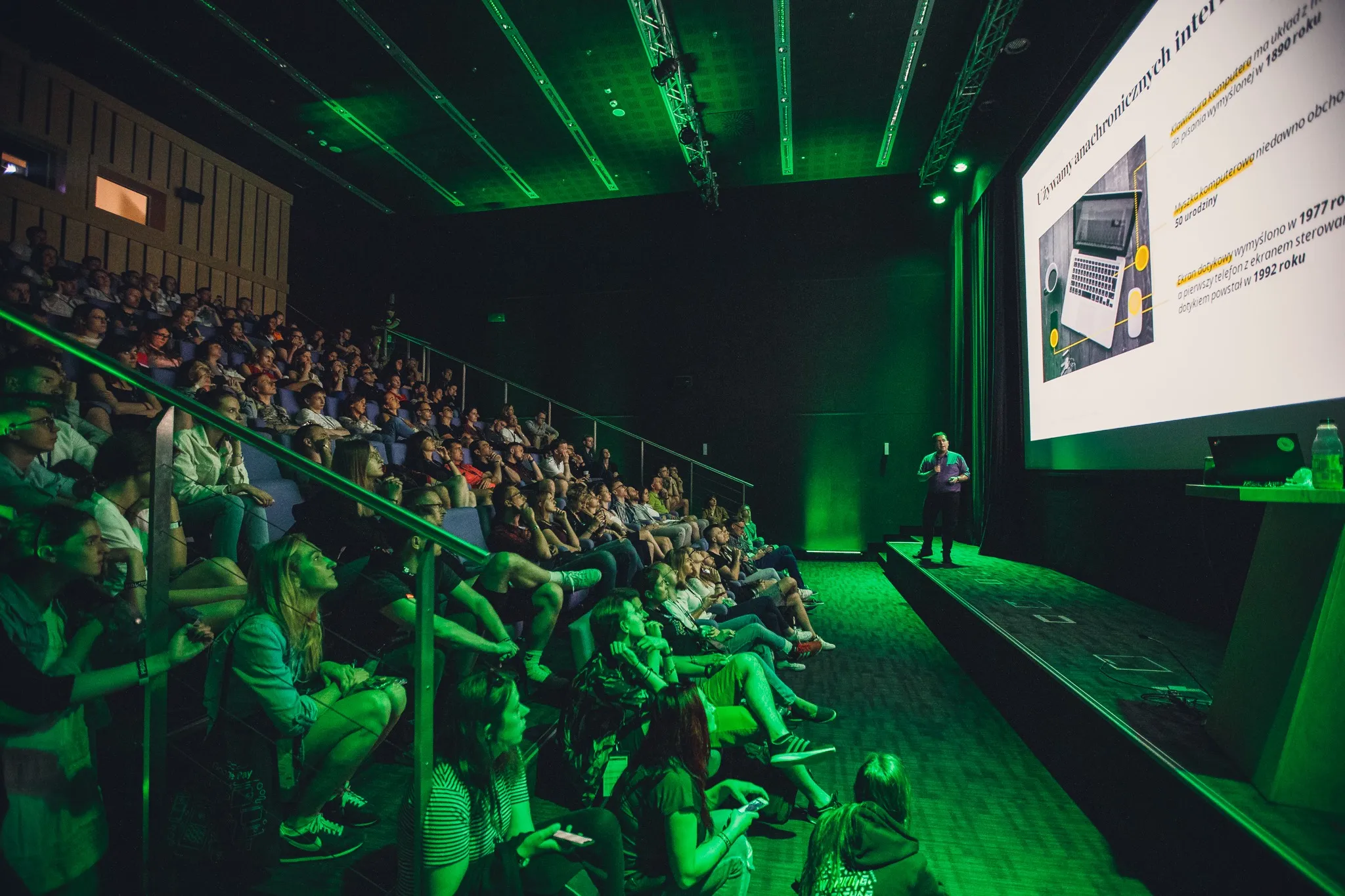 Conference audience in a hall lit green, with a projected screen on stage